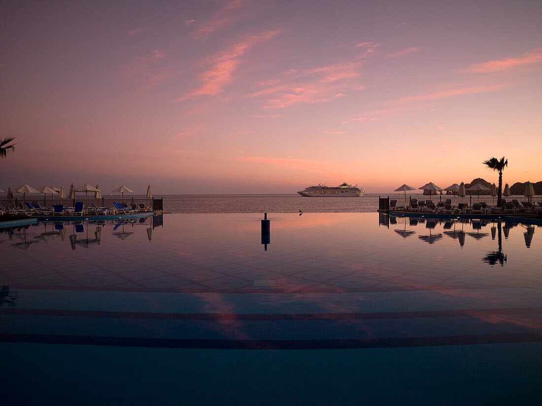 Swimmingpool in einer Ferienanlage in der Abenddämmerung, Kreuzfahrtschiff im Hintergrund; Los Cabos, Mexiko
