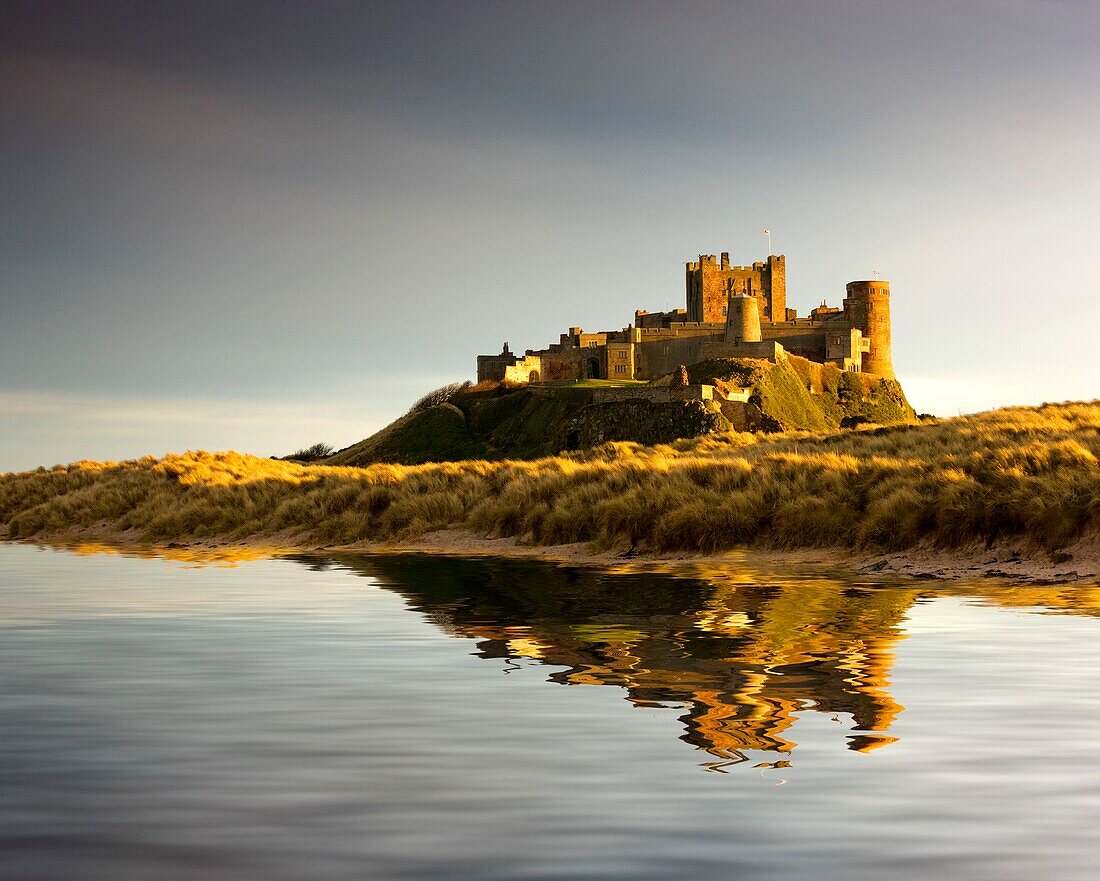 Bamburgh Castle, mit einem Spiegelbild im Wasser. Beachten Sie, dass die Wasserspiegelung falsch ist und das Ergebnis einer Bildmanipulation ist; Bamburgh, Northumberland, England