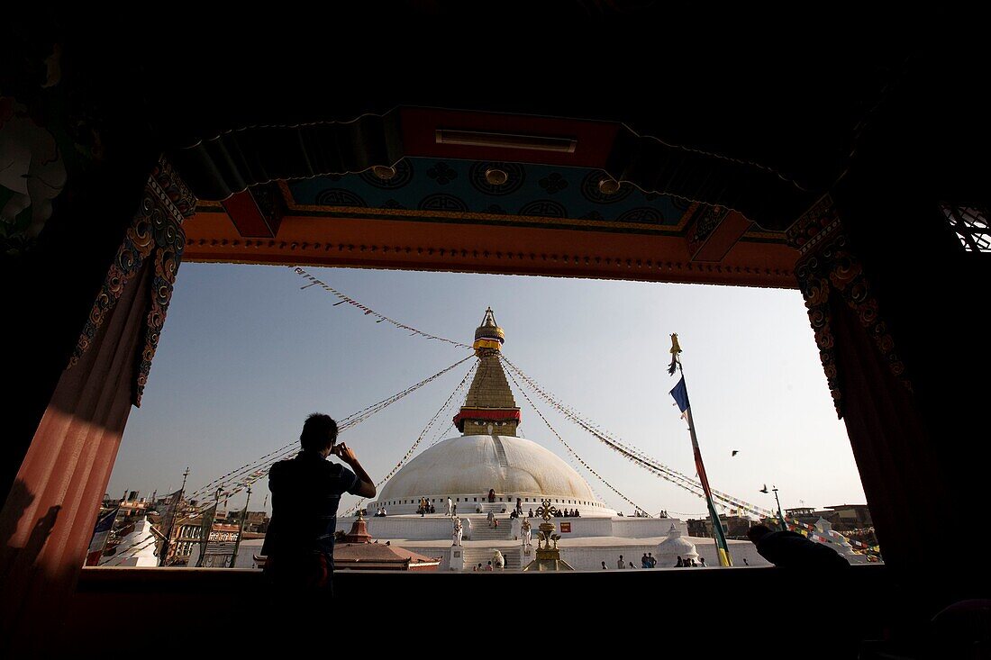 Ein Mann, der die Boudhanath Stupa durch ein Fenster fotografiert