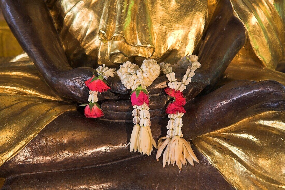 Wat Somdej Phuttachan, Thailand; Nahaufnahme von geblümten Leis über der Hand einer buddhistischen Statue