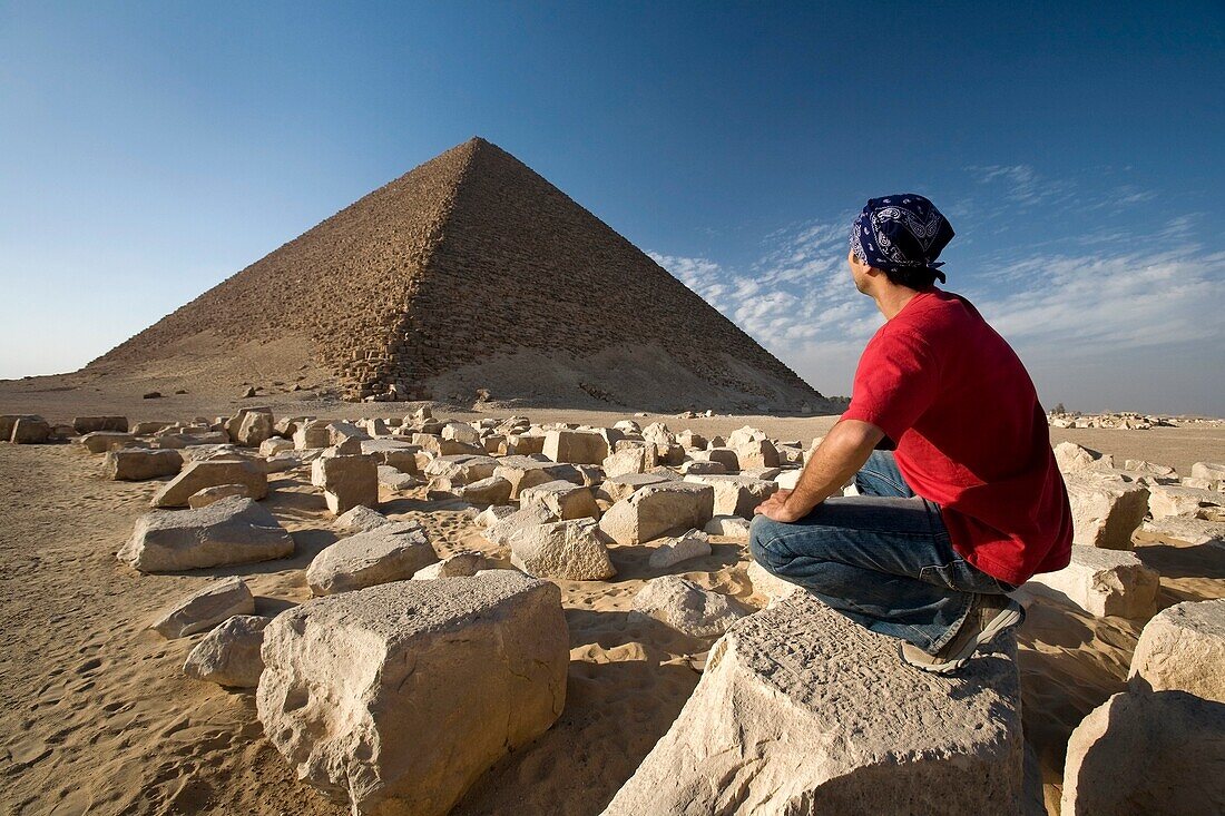 Ein Mann kauert in der Nähe einer Pyramide in der Wüste