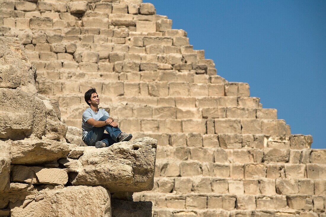 Mann, der auf einem Teil einer Pyramide in der Wüste sitzt; Kairo, Ägypten, Afrika