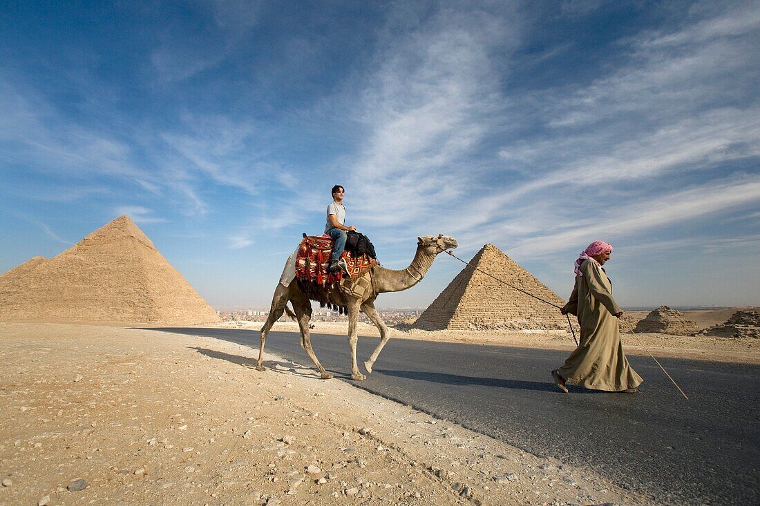 Ein Führer, der ein Kamel und einen Passagier zu den Pyramiden führt; Kairo, Ägypten, Afrika