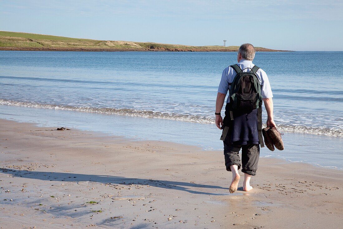 Mann geht am Strand spazieren; Northumberland, England