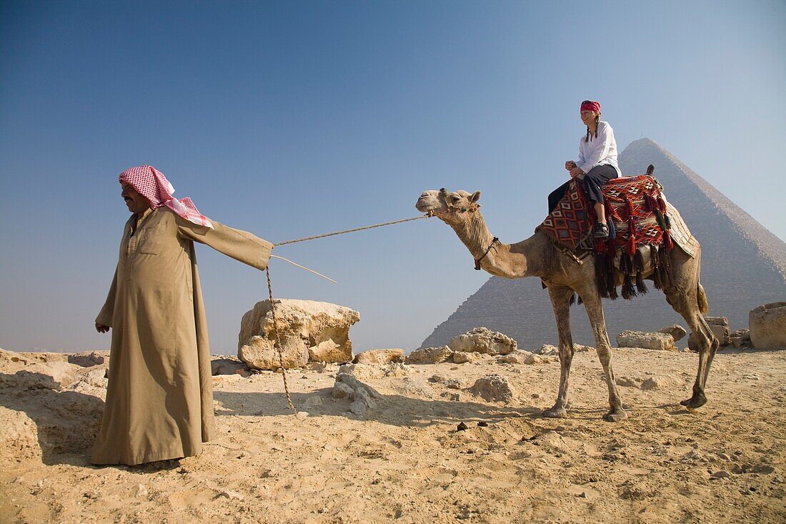 Young Woman Tourist On A Camel Being Led By A Guide At The Pyramids Of Giza, Cairo, Egypt