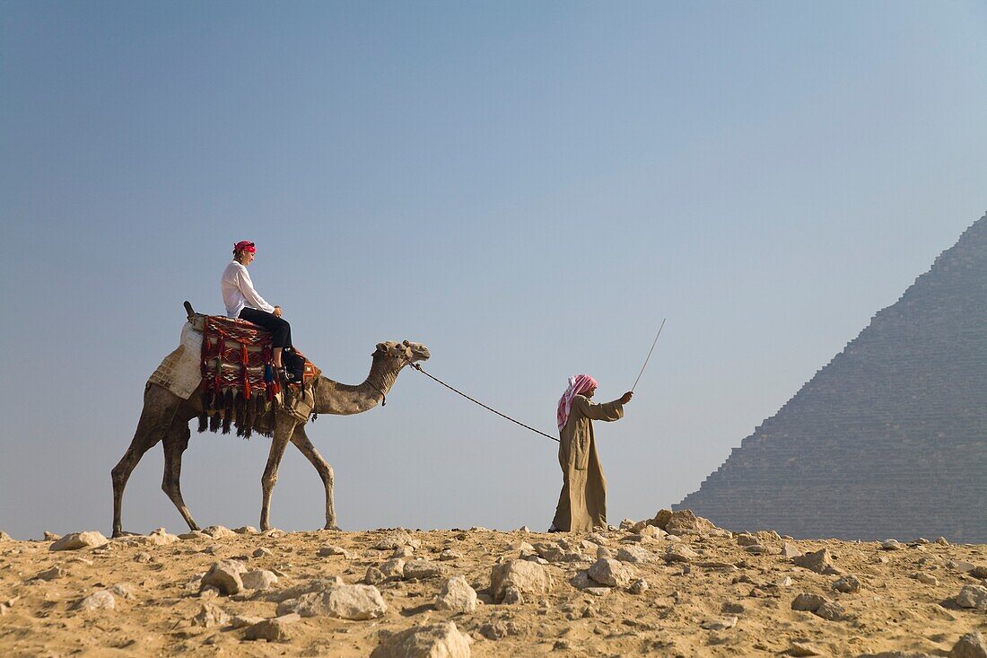 Junge Touristin auf einem Kamel, geführt von einem Führer, bei den Pyramiden von Gizeh, Ägypten