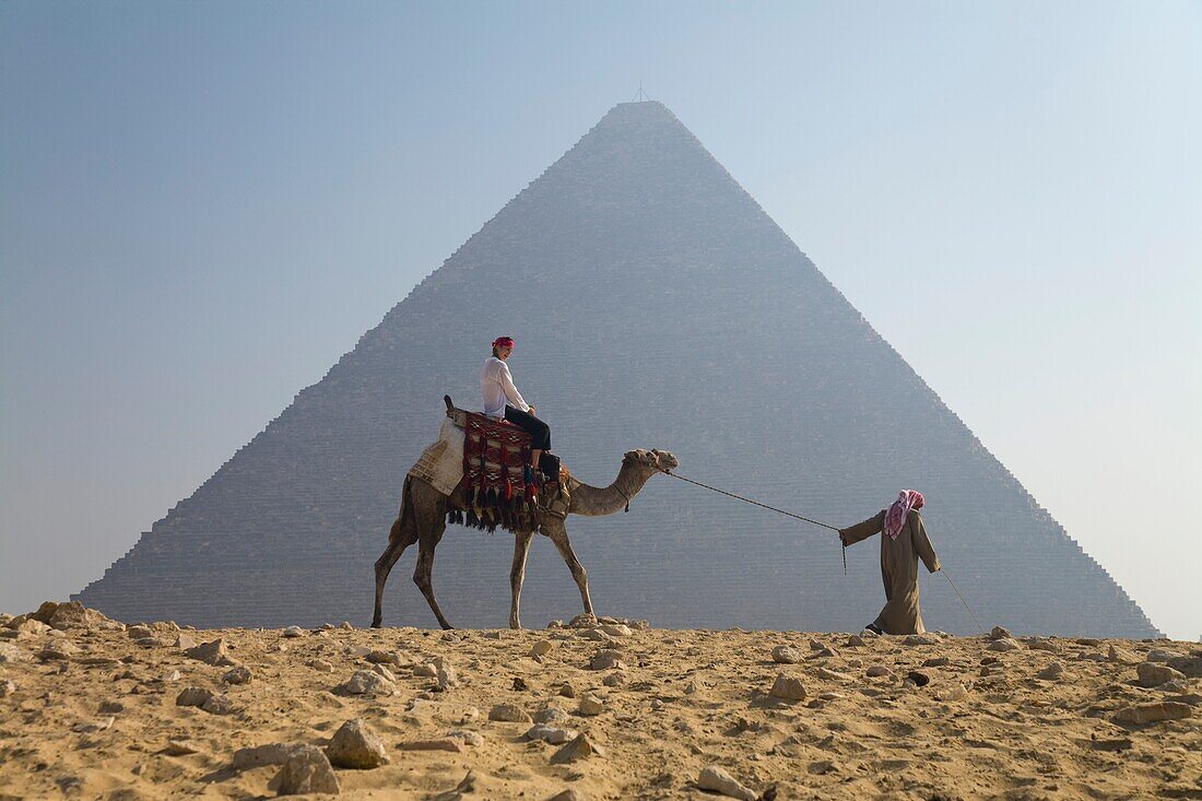 Junge Touristin auf einem Kamel, geführt von einem Führer bei den Pyramiden von Gizeh; Kairo, Ägypten, Afrika