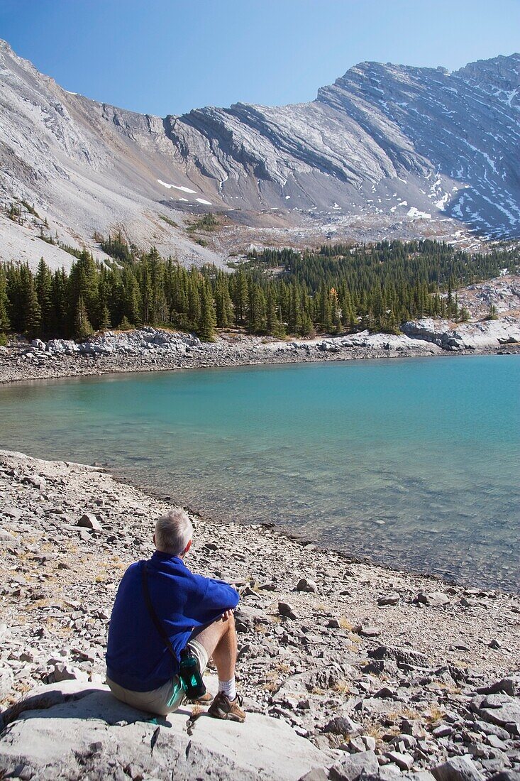 Mann neben einem Bergsee sitzend