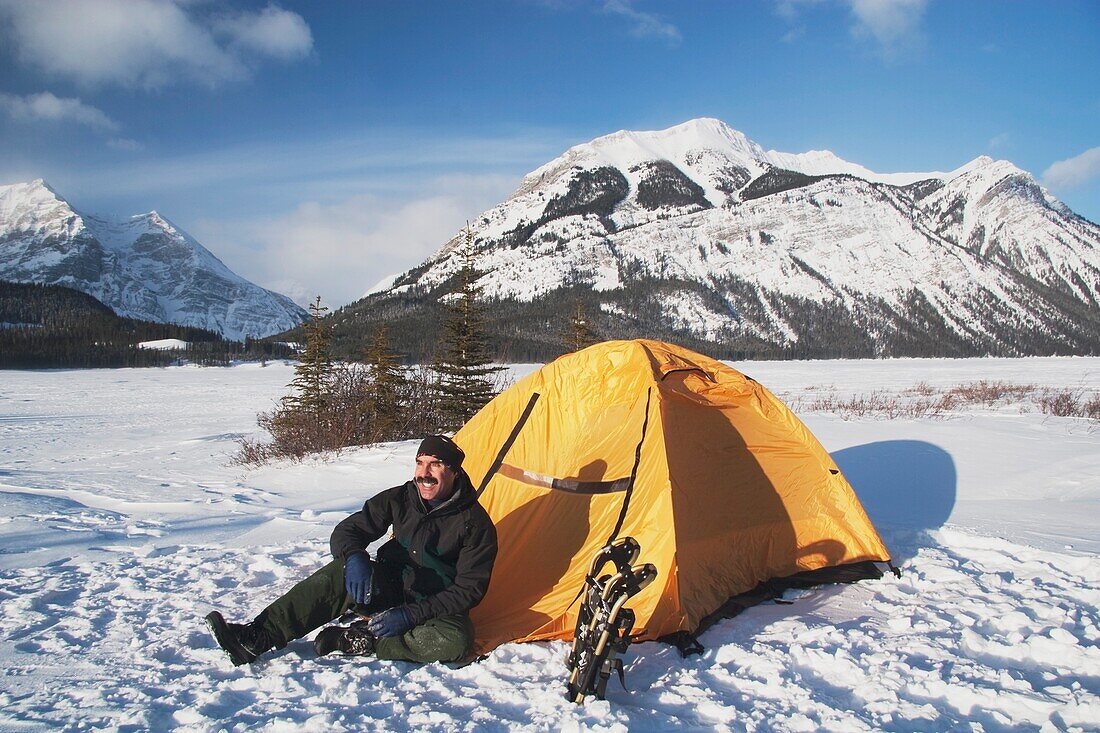 Mann sitzt bei seinem Zelt im Schnee im Winter