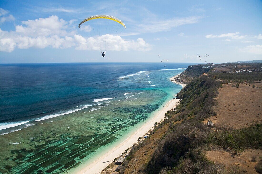 Ein Gleitschirmflieger schwebt frei über den Klippen und Stränden der Bukit-Halbinsel in Bali, Indonesien