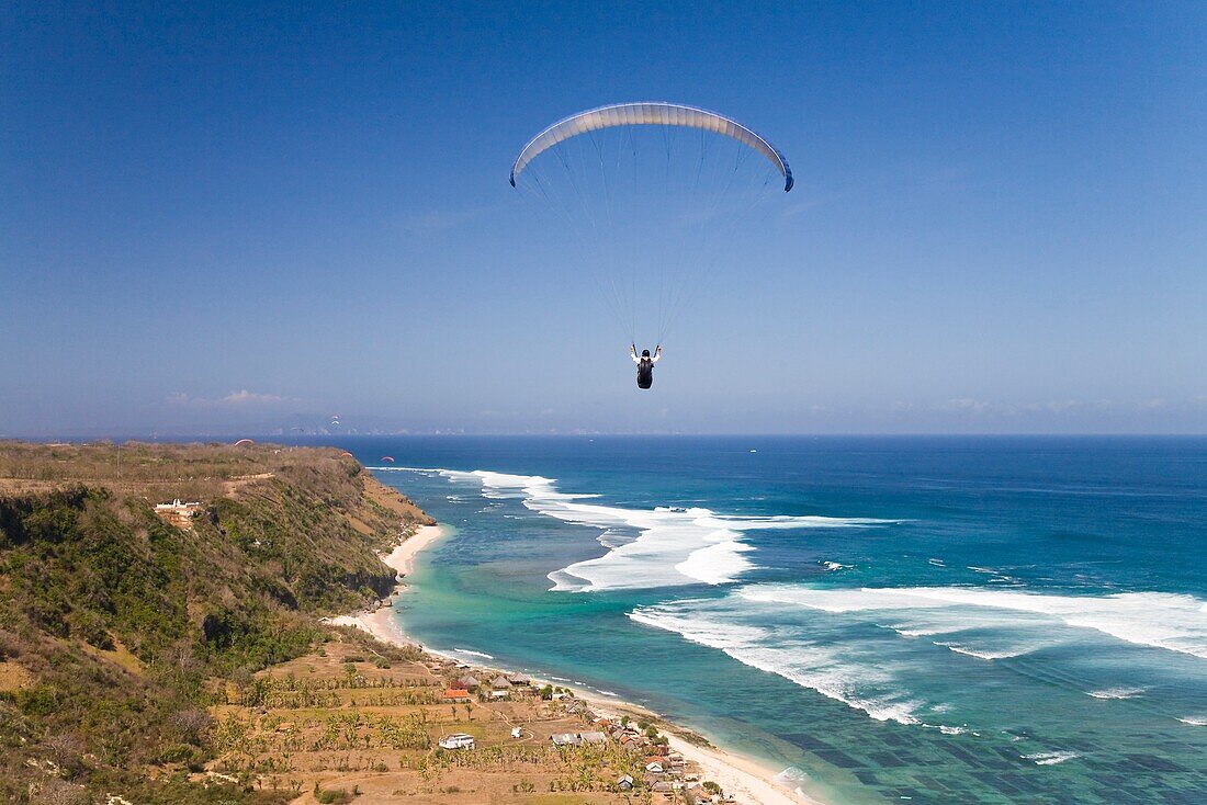 Ein Gleitschirmflieger schwebt frei über den Klippen der Bukit-Halbinsel in Bali; Bali, Indonesien