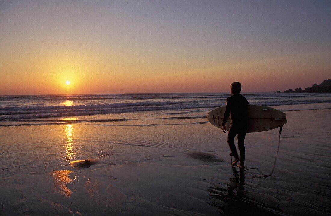 Silhouettierter Surfer am Sandstrand bei Sonnenuntergang