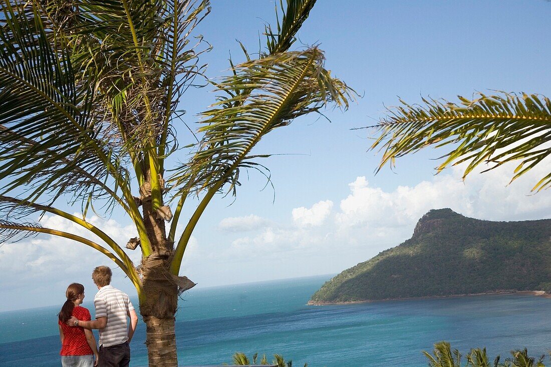 Paar steht bei einer Palme und überblickt Insel und Küste