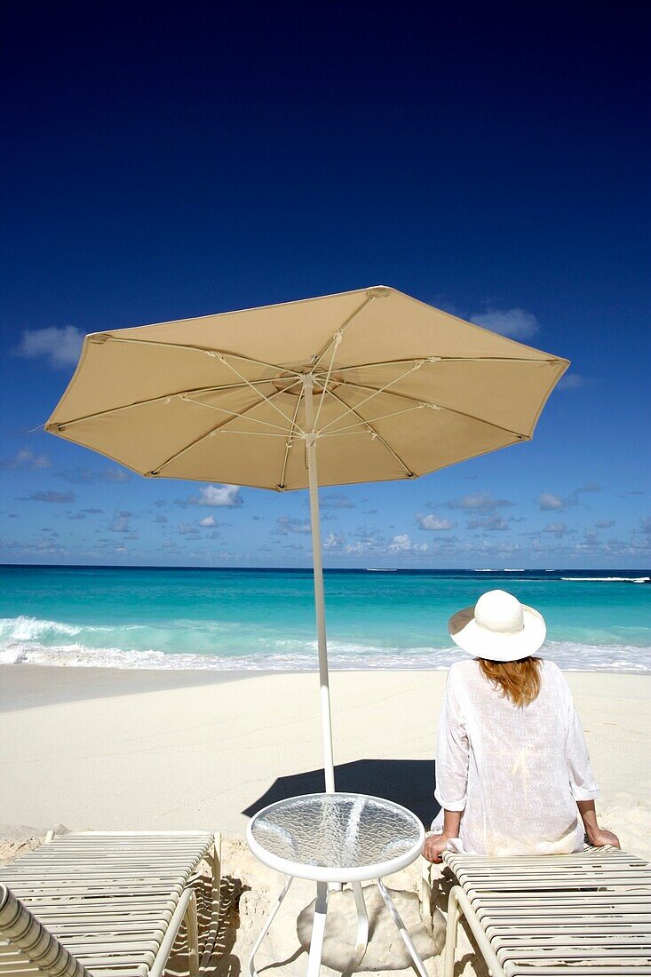 Woman On Beach Sitting On Sunlounger Under Umbrella