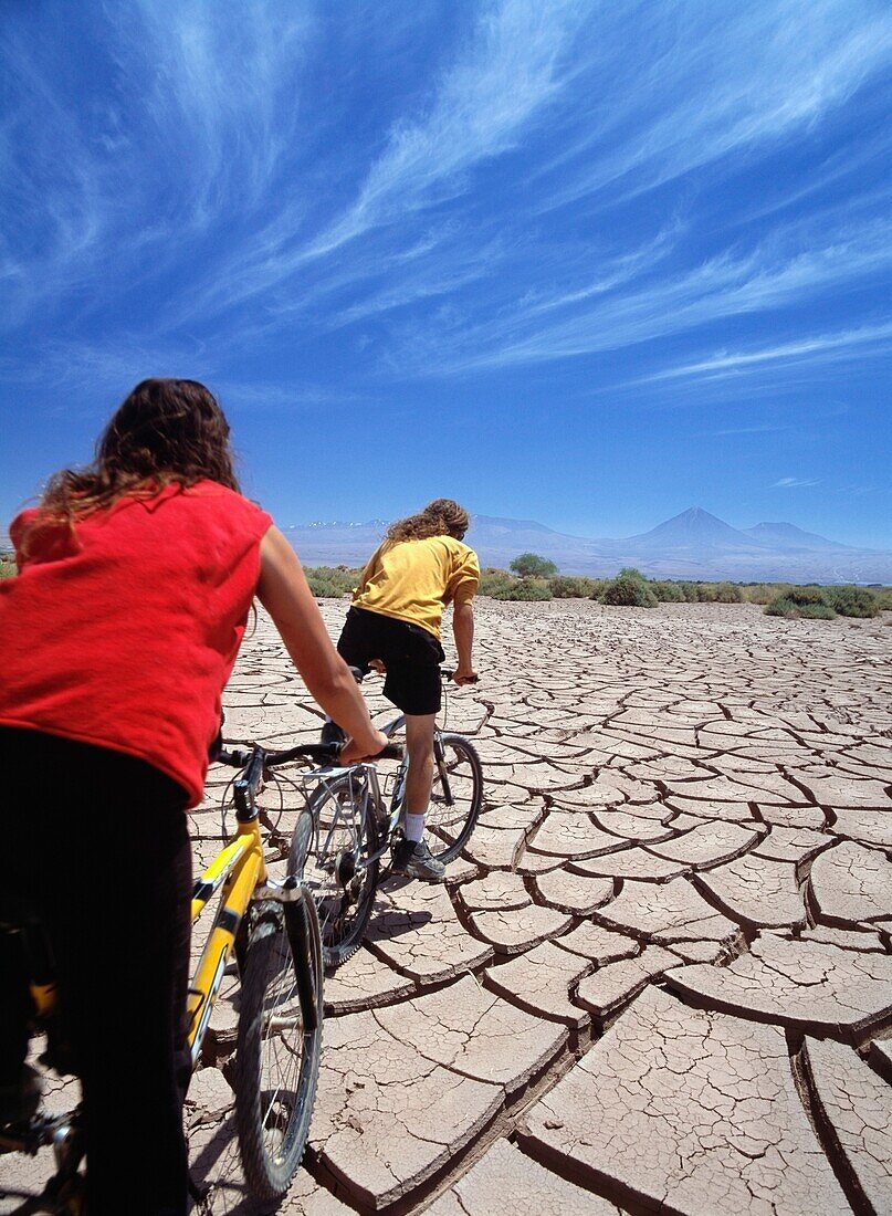 Two Cyclists Travelling Over Cracked Mud In The Atacama Desert