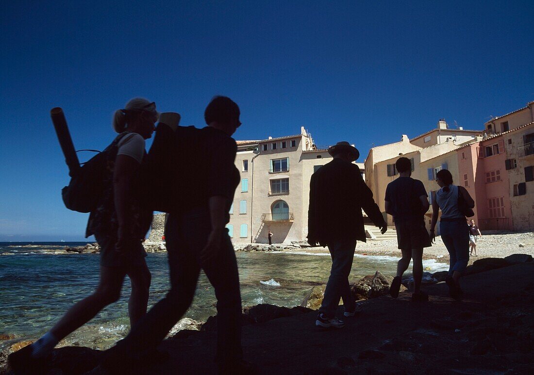 Silhouettes Of People Walking Along Beside Small Beach; St Tropez, France