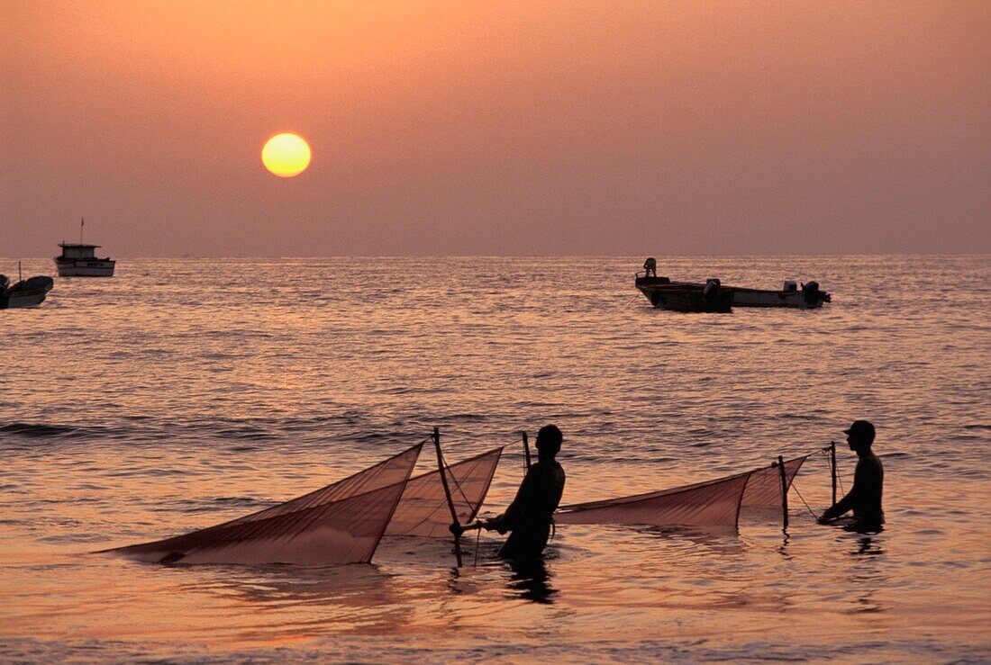 Fischer mit Netzen im Meer bei Sonnenuntergang