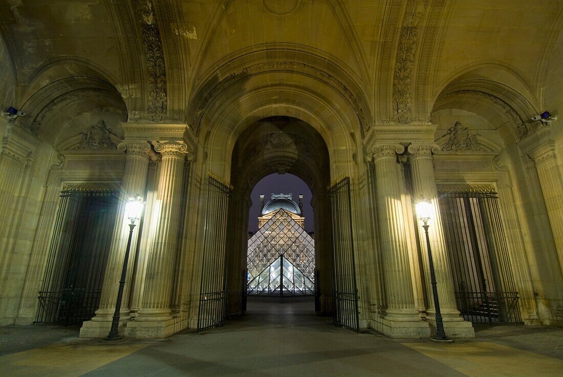Blick durch die Passage Richelieu des Louvre-Museums auf die Glaspyramide bei Nacht.