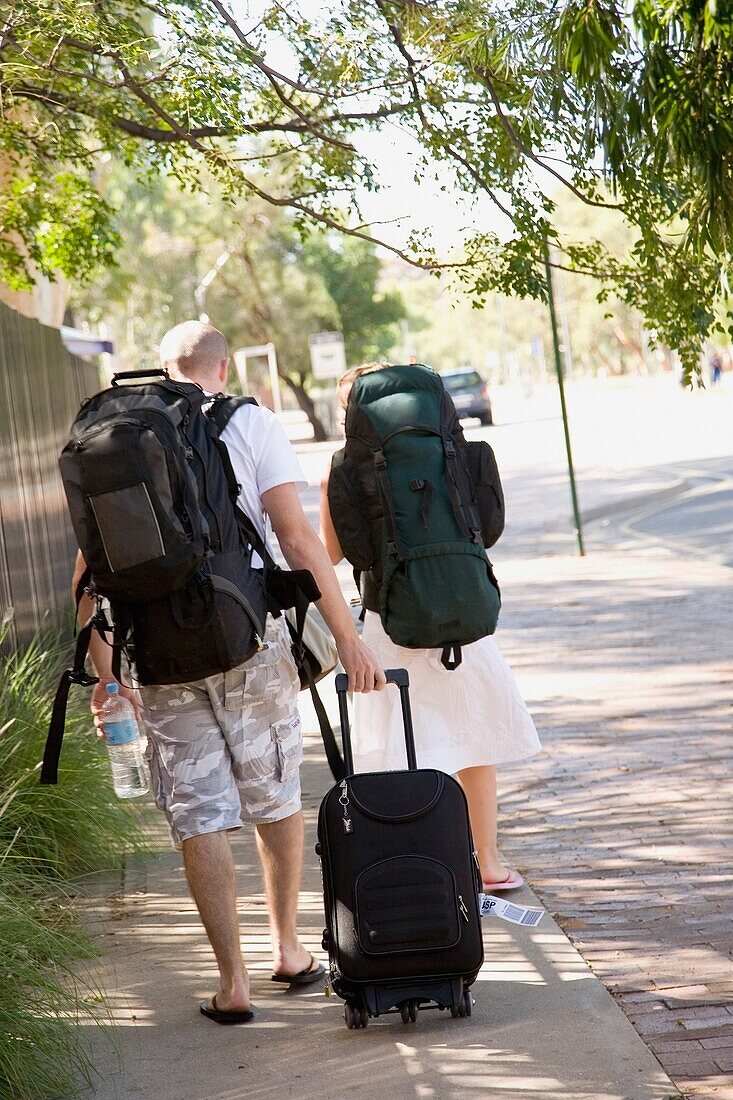 Young Couple Walking Down Street With Backpacks And Suitcase