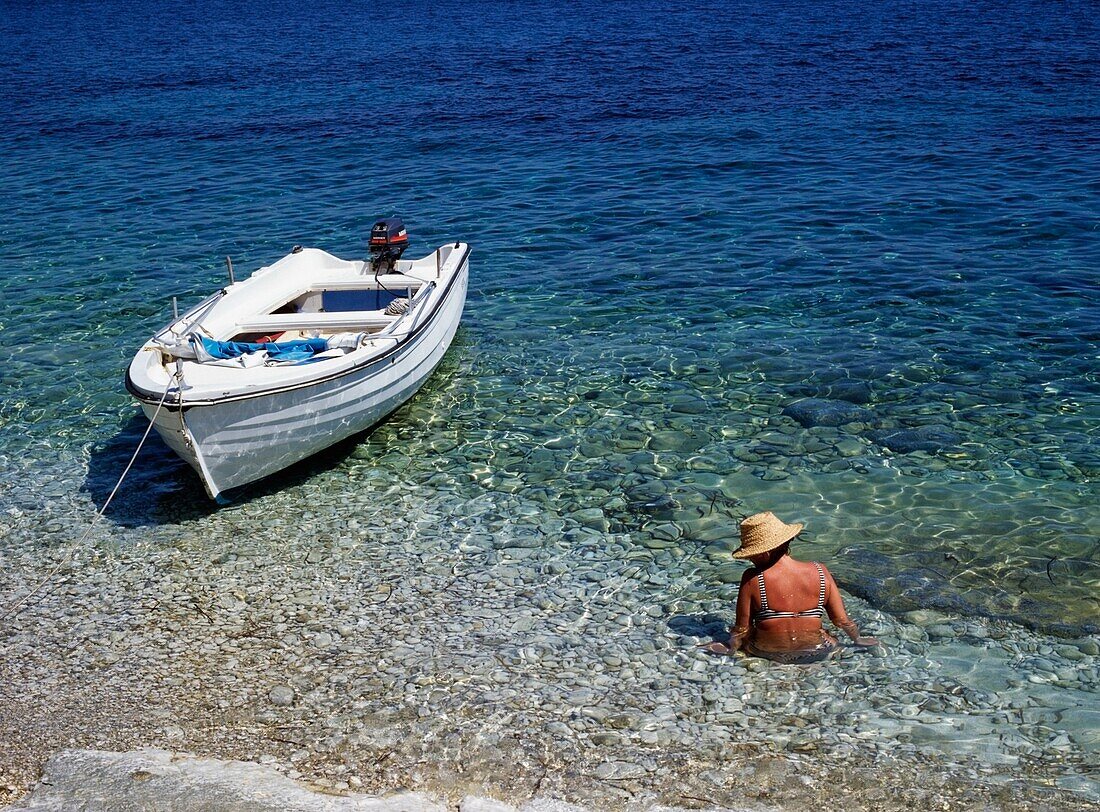 Frau watet im Wasser neben einem Boot, Korfu
