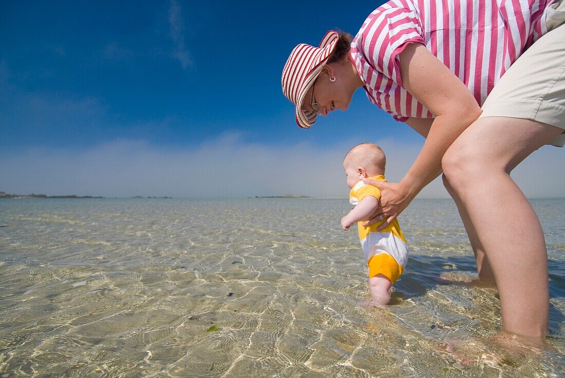 Mutter und Baby in seichtem Wasser vor dem Strand, Blickwinkel niedrig