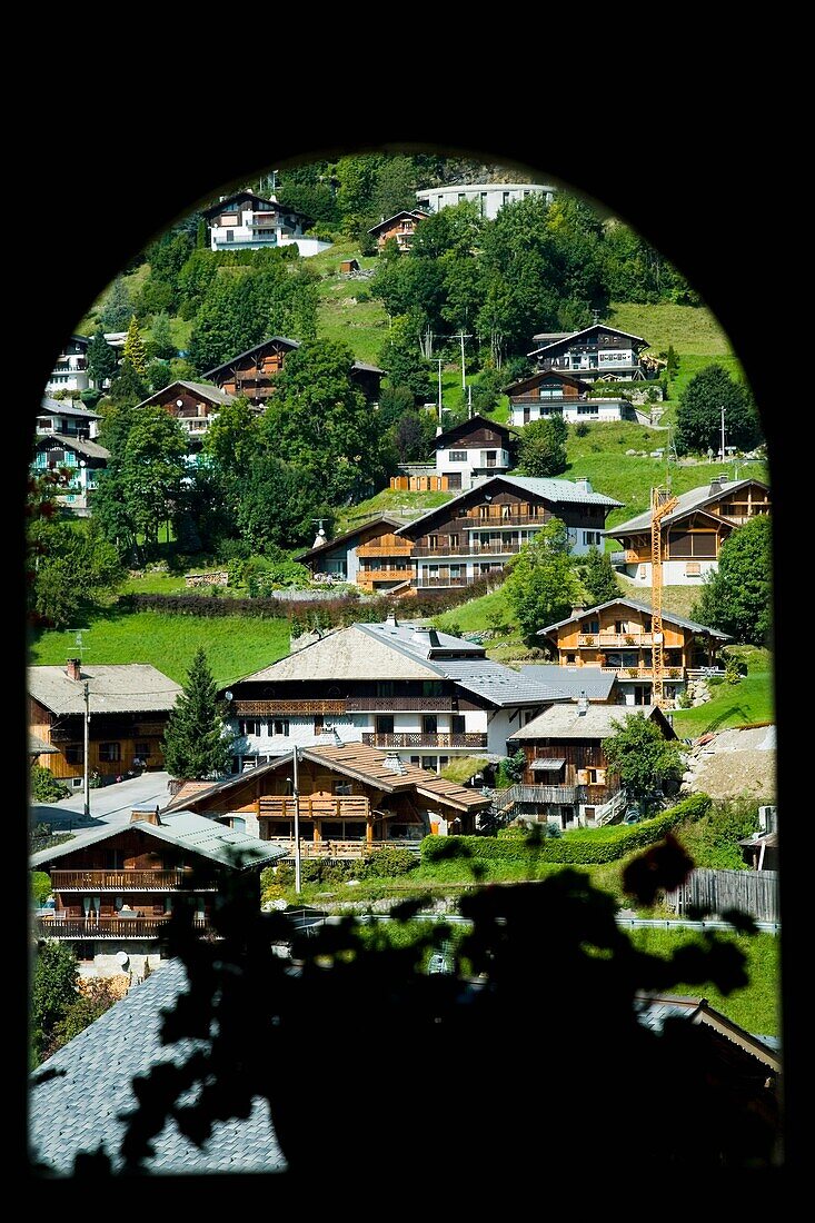 View Through Arched Window Of Alpine Lodges And Chalets On Hillside