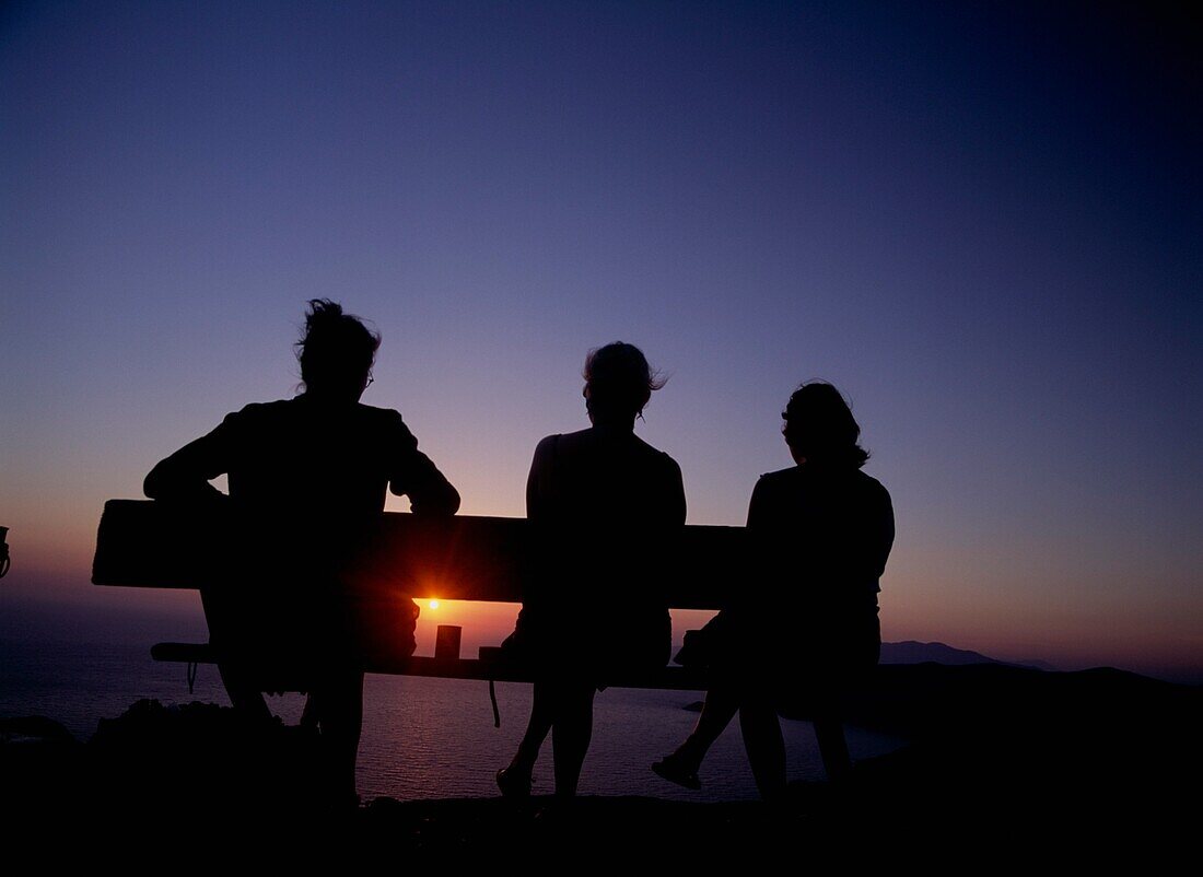 Drei Frauen beobachten den Sonnenuntergang über der Küste