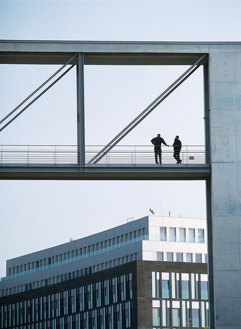 Two Men On Bridge Between Government Buildings Either Side Of River Spree