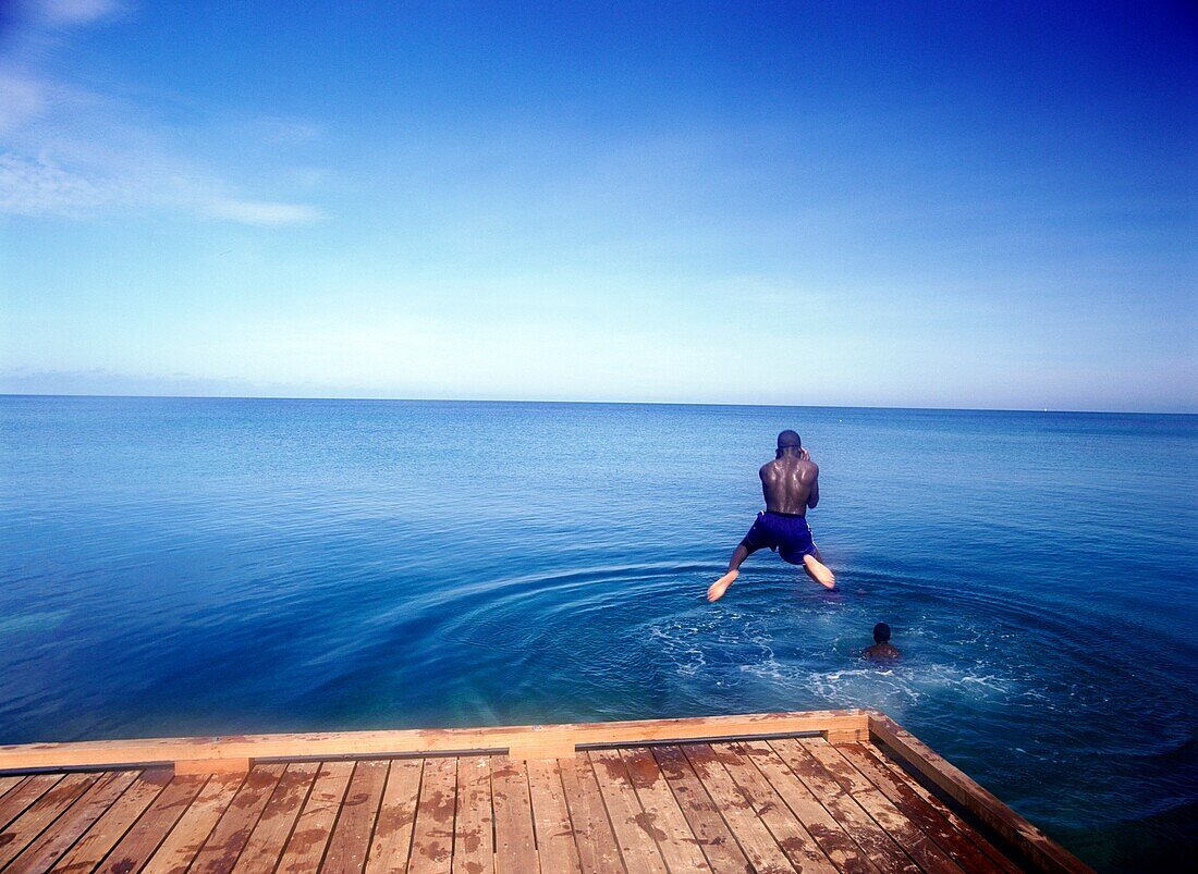 Junger Junge springt vom Pier ins Wasser von Grand Anse Beach