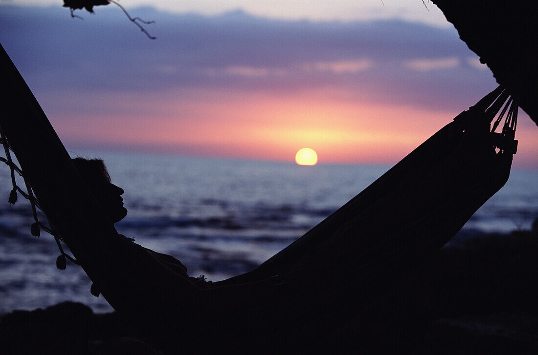 Frau auf Hängematte am Strand bei Sonnenuntergang liegend