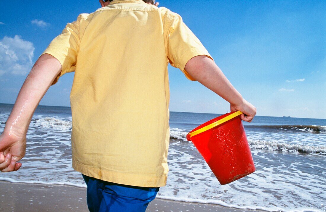 Junge spielt am Strand und trägt einen Eimer