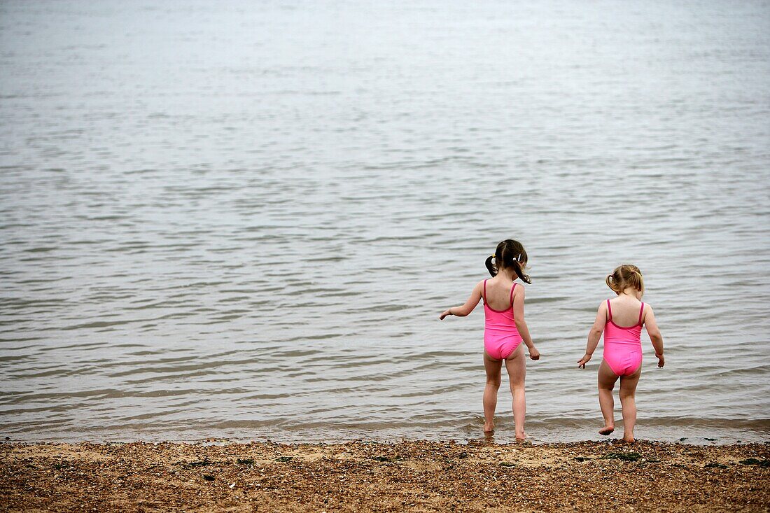 Schwestern in passenden rosa Badeanzügen beim Spielen am Strand