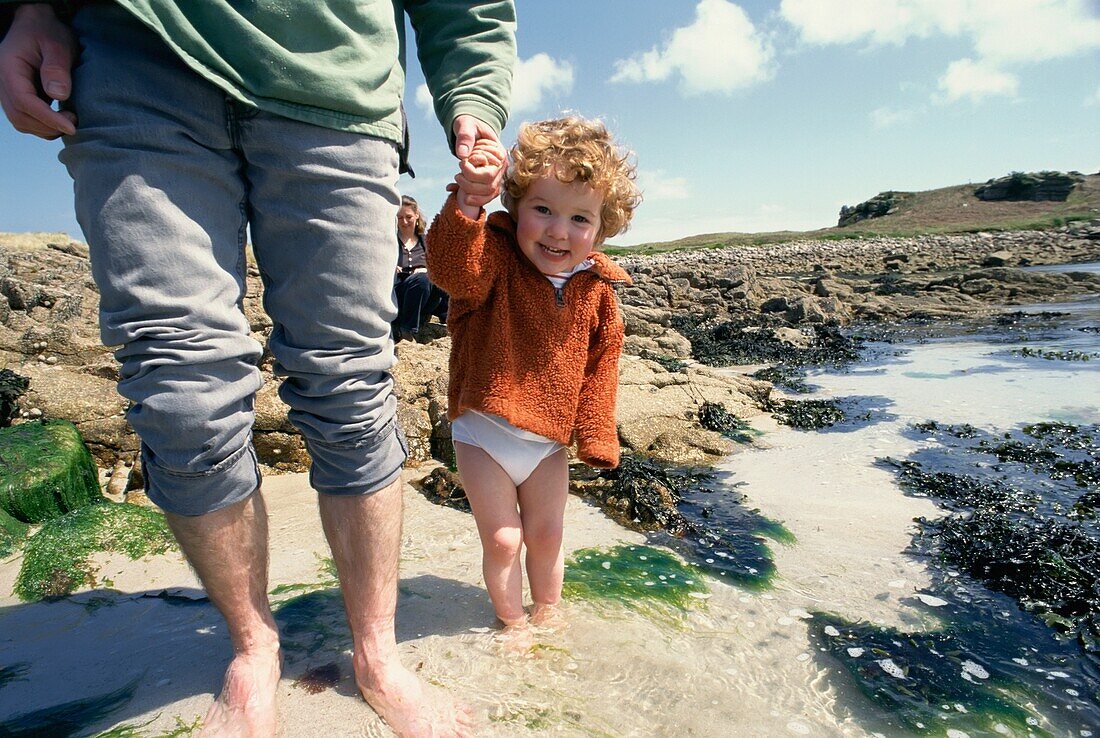 Junges Mädchen hält die Hand der Eltern am Strand