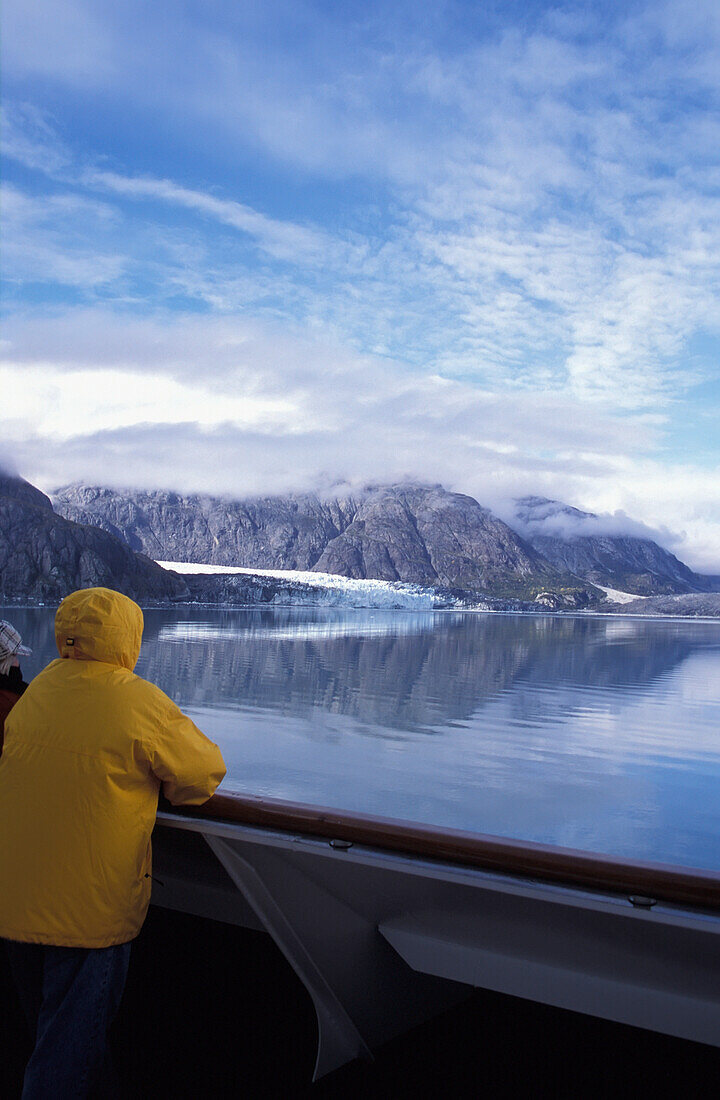 Tourist steht an der Reling eines Kreuzfahrtschiffes und schaut auf den Gletscher