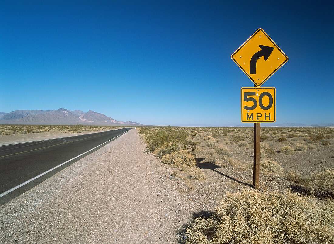 Road Sign Beside Road Running Through The Mojave Desert