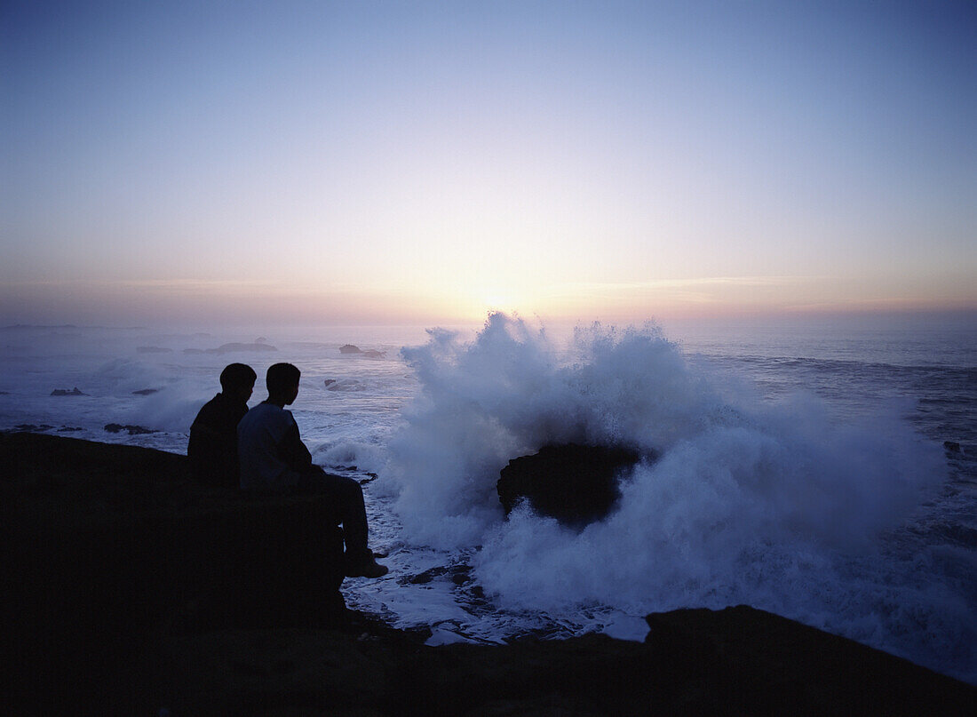 Zwei Jungen beobachten die Wellen, die in der Abenddämmerung gegen die Felsen und Mauern von Essaouira prallen