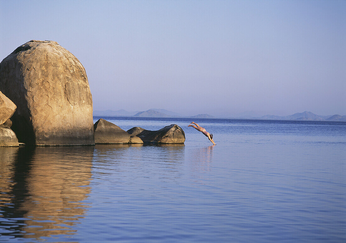 Frau taucht in der Abenddämmerung vor der Insel Mumbo in ruhiges Wasser