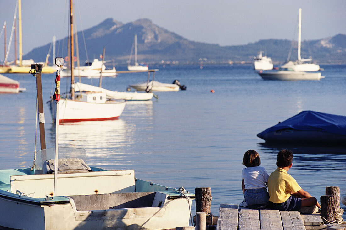 Zwei kleine Kinder sitzen auf einem Dock in Port De Mollenca
