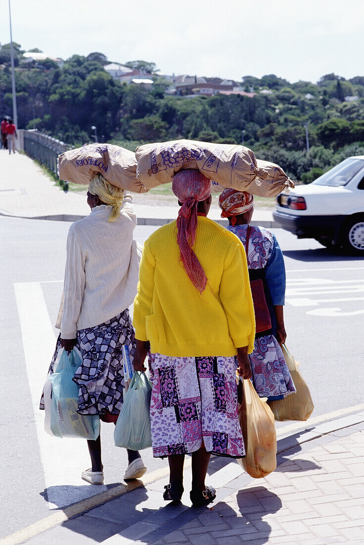 Frau mit Säcken auf dem Kopf beim Überqueren der Straße mit Einkäufen