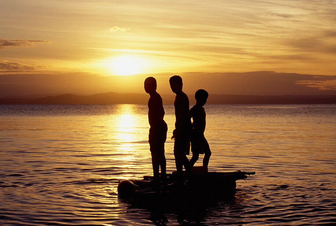 Silhouette Of Young Boys On Boat At Sunset