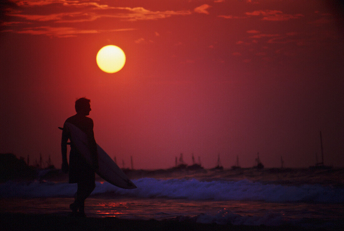 Surfer hält Surfbrett bei Sonnenuntergang
