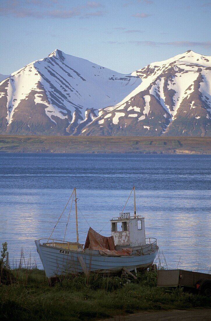 Fischerboot am See und schneebedeckte Berge