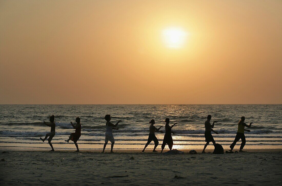 Silhouetten von Menschen, die Tai Chi am Meer am Strand bei Sonnenuntergang machen