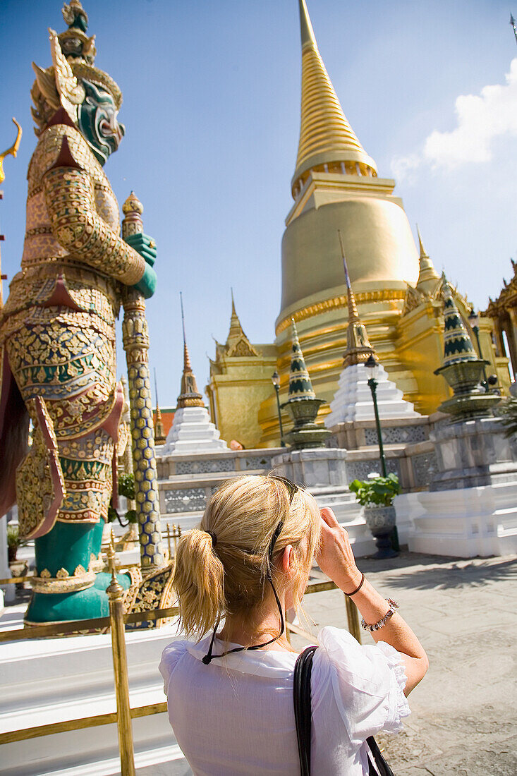 Touristin im Grand Palace vor dem goldenen Phra Sri Ratana Chedi und der wachsamen Yaksha-Demo