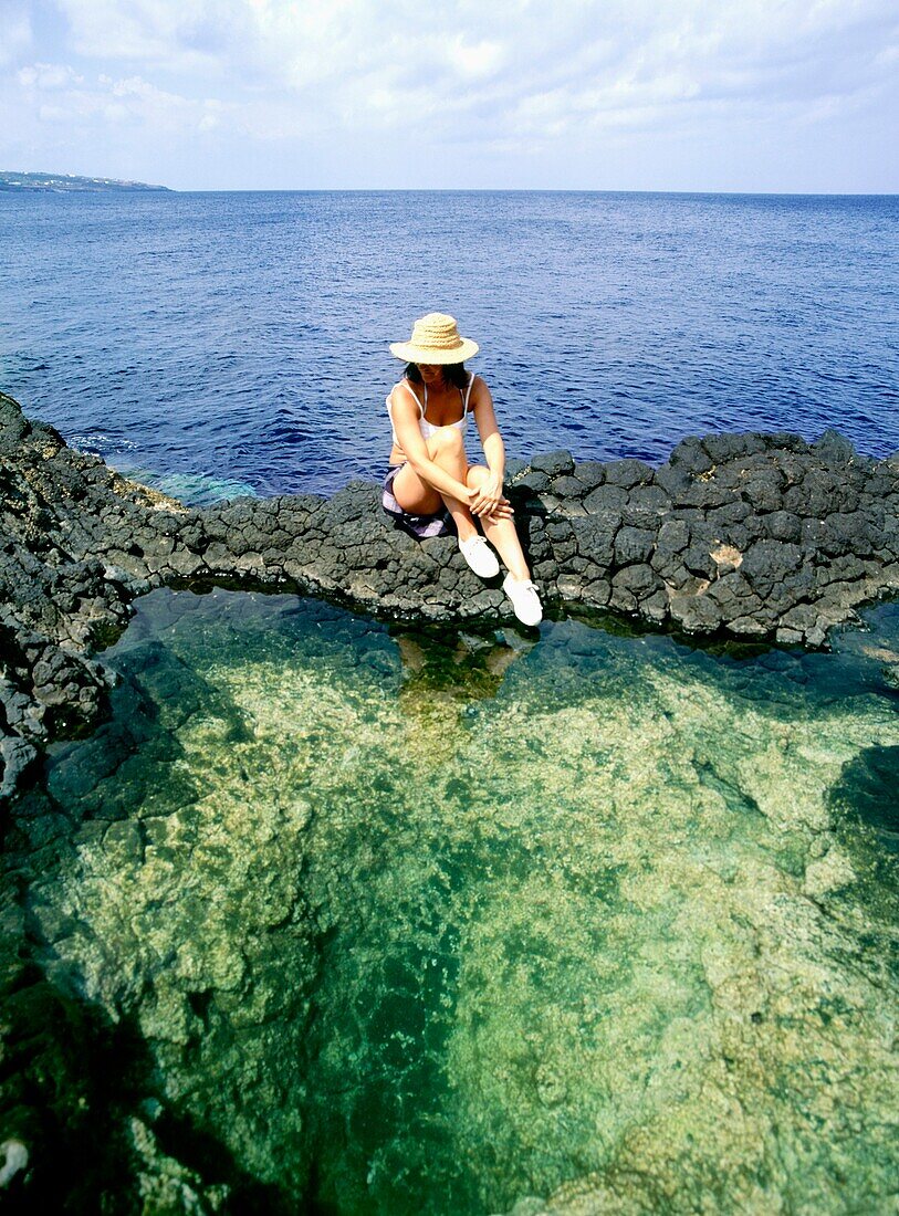 Woman Sitting By Rock Pools With Sea Behind