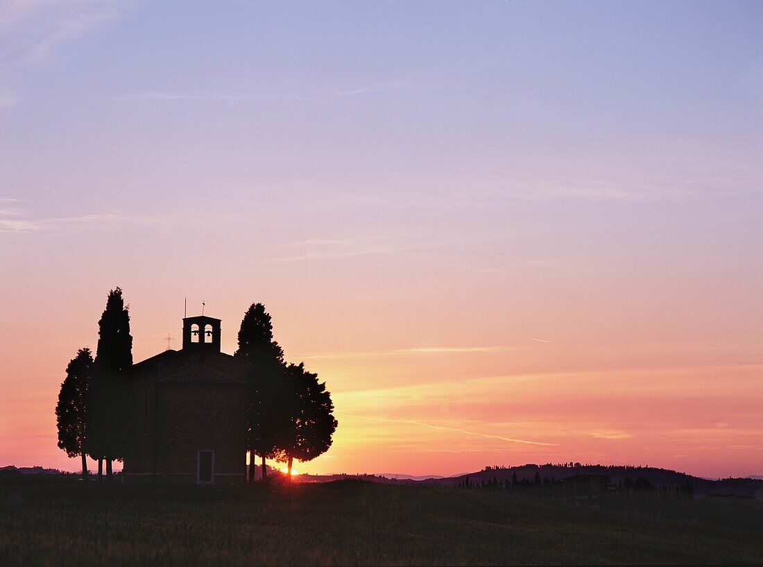 Zypressen neben einer kleinen Kapelle in der Abenddämmerung bei San Quirico D'orcia