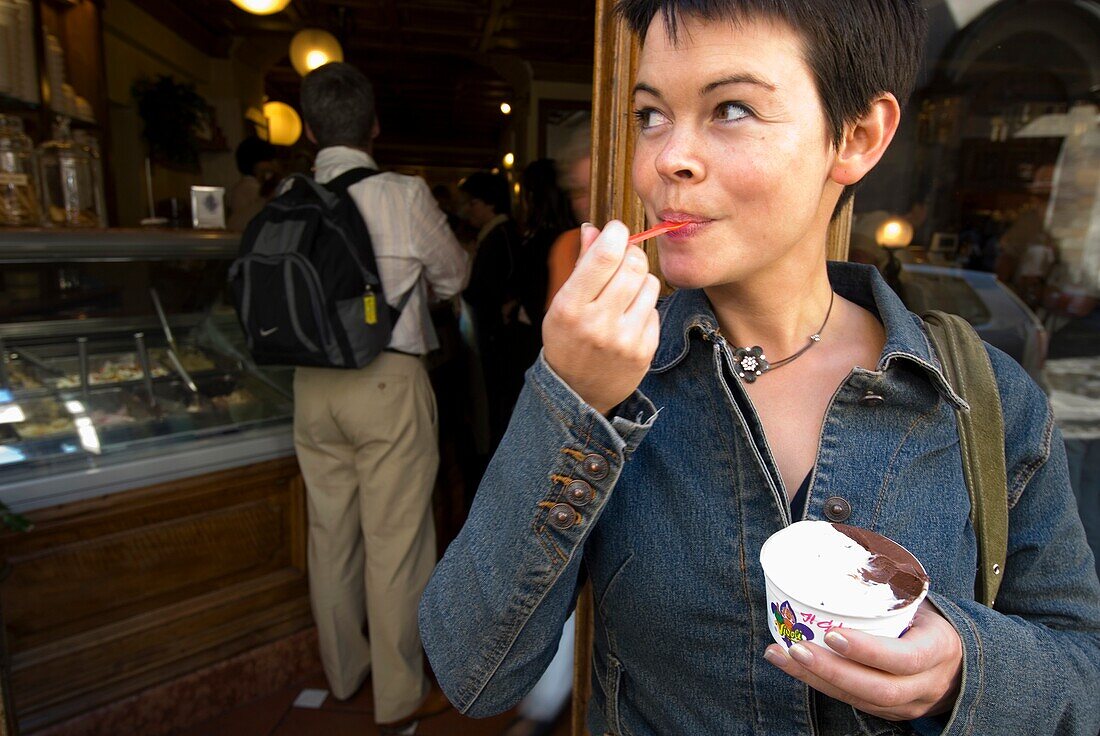 Frau isst Eiscreme außerhalb einer Gelaterie