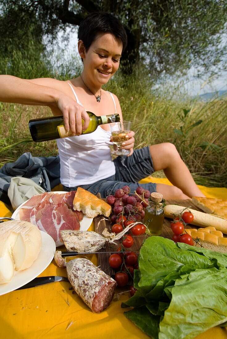 Frau gießt eine Flasche Wein in Vorbereitung auf ein Picknick unter Olivenbäumen ein
