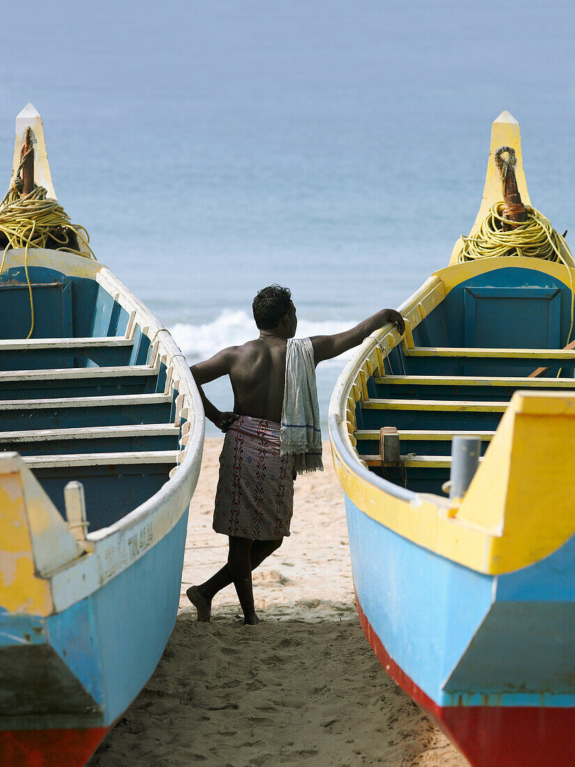 Man Leaning On Fishing Boats On Beach