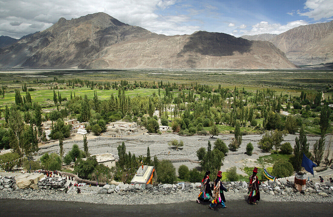 Frauen in traditioneller Kleidung wandern entlang einer Straße am Fuße der Berge